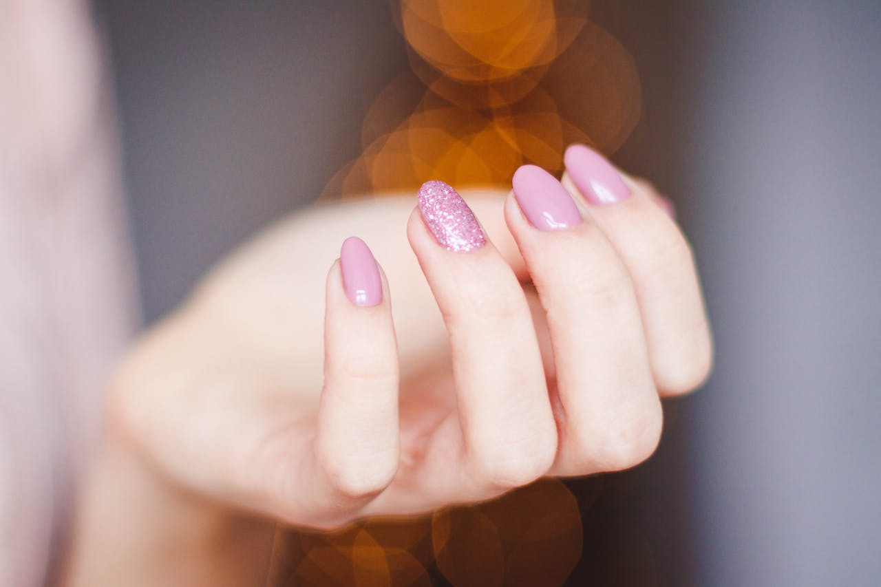 our-mission A close-up of a womans hand displaying a stylish pink glitter manicure, highlighting nail art details.