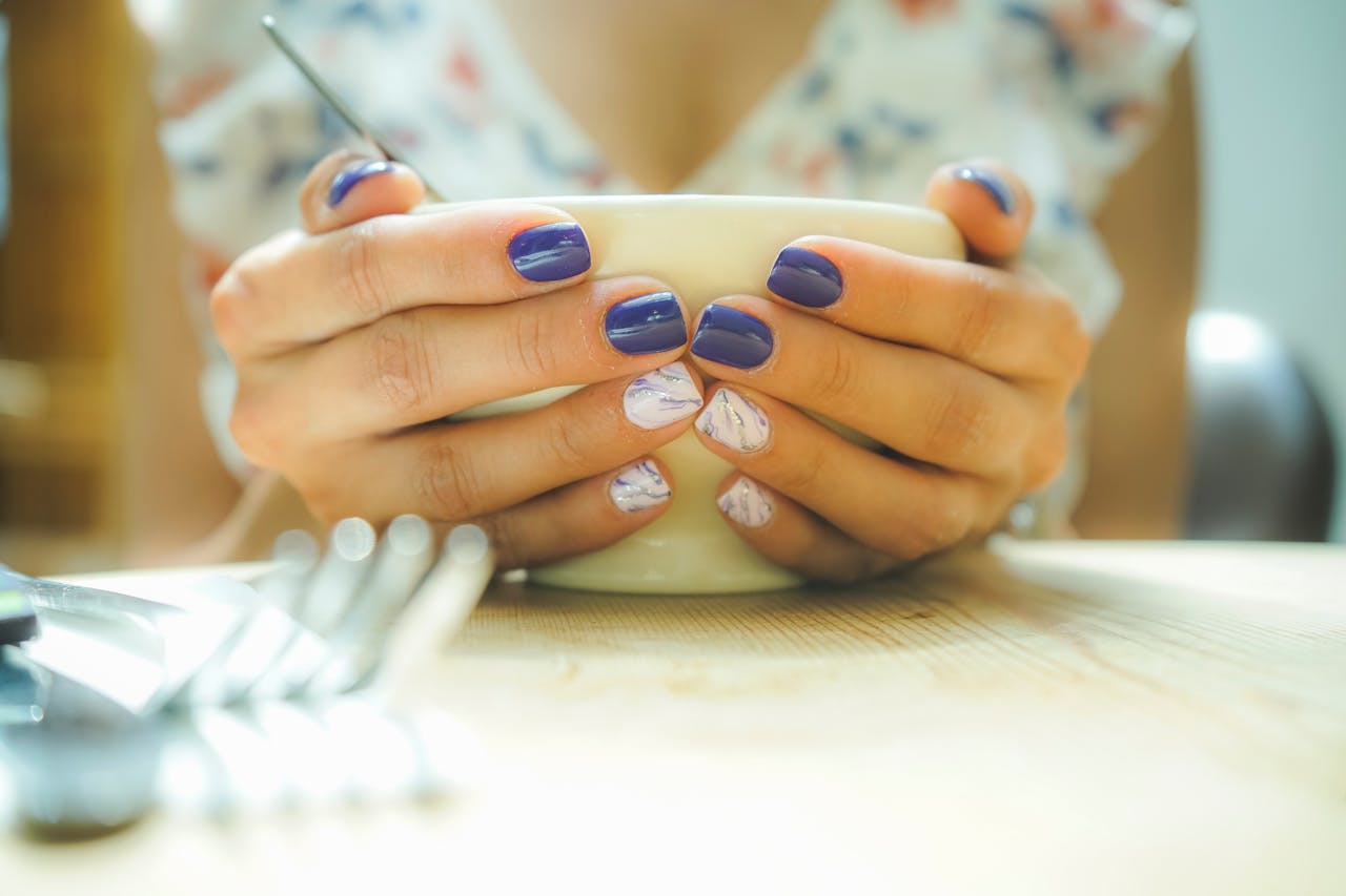 portfolio-05 A woman with colorful nails holds a mug, capturing a moment of warmth and style indoors.