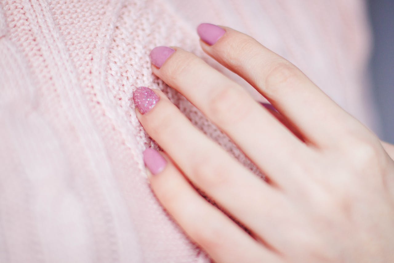 portfolio-06 Close-up of a womans hand with pink manicure resting on a soft knit sweater, showcasing elegance and fashion.